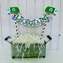 Load image into Gallery viewer, Recycling trash truck cake topper featuring two green trash trucks, pennant with green letters strung between black and white striped paper straws. There are two blue recycling trash bins on the beginning and end letters on the cake bunting cake topper.