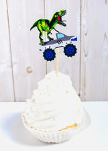 Load image into Gallery viewer, Monster jam inspired monster trucks with a T-Rex dinosaur cupcake toppers. Each monster truck features a T-Rex standing on the back of the truck. The monster truck dinosaur cupcake toppers are professionally printed, cut and attached to four inch bamboo skewers. The monster truck dinosaur cupcake toppers are handcrafted in the USA. The truck options are Grave Digger, Megaladon, El Toro Loco, Tornado and Dragon.