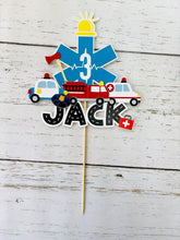 Load image into Gallery viewer, The first responders cake topper features a police car, firetruck, ambulance, road letters, EMT emblem with age and heart beat monitor with a yellow siren.