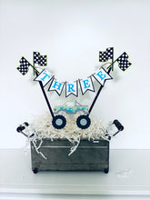 Load image into Gallery viewer, Pink monster truck cake topper. The cake topper is customizable and can display an age, name, word or phrase. The colors are also customizable. The pink monster truck cake topper features two checkered flags, pennant banner and a monster truck to display underneath the bunting. The pink monster truck cake topper is designed and handcrafted by Laura, the owner of Declan & Smith Party Decor.