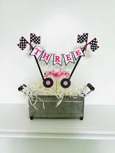 Load image into Gallery viewer, Pink monster truck cake topper. The cake topper is customizable and can display an age, name, word or phrase. The colors are also customizable. The pink monster truck cake topper features two checkered flags, pennant banner and a monster truck to display underneath the bunting. The pink monster truck cake topper is designed and handcrafted by Laura, the owner of Declan & Smith Party Decor.