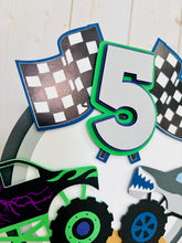 Load image into Gallery viewer, Monster jam inspired dueling monster truck cake topper. The monster jam cake topper features two monster trucks, a checkered flag, dirt mounds, age for the birthday boy or girl and the birthday kiddo's name. The monster jam cake topper is customizable.