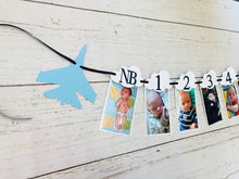 Load image into Gallery viewer, Top Gun fighter jet themed first birthday photo banner. The top gun photo banner features two fighter jets flanking 13 white clouds. The clouds are numbered NB - 12 months for a first birthday. The numbers can be customized to fit any age birthday. The planes, number colors and ribbon color is customizable.