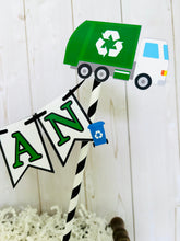 Load image into Gallery viewer, Recycling trash truck cake topper featuring two green trash trucks, pennant with green letters strung between black and white striped paper straws. There are two blue recycling trash bins on the beginning and end letters on the cake bunting cake topper.