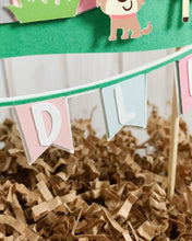 Load image into Gallery viewer, The pink barnyard farm animals cake topper features a pink barn, pink tractor, white picket fence, farm animals and a pink and light blue pennant banner to display your little one's name.