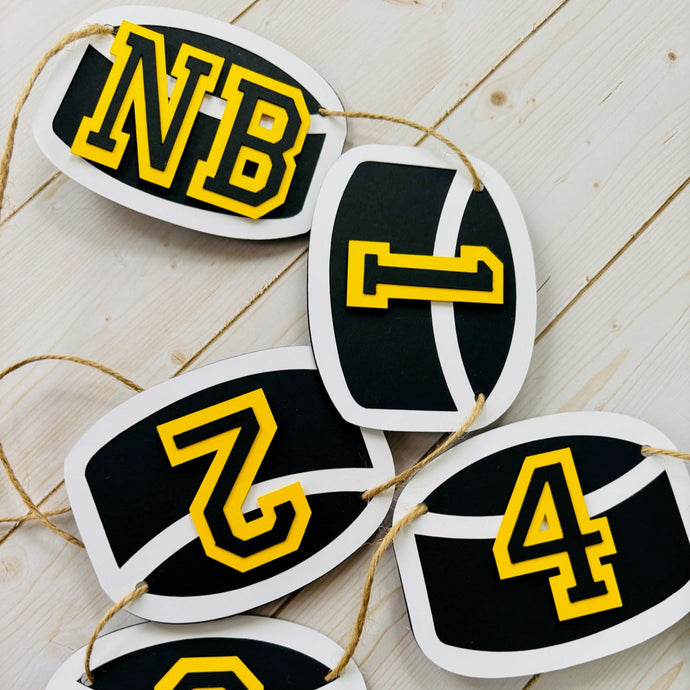 Hockey puck first birthday photo banner featuring 13 hockey pucks. Each hockey puck is sized to fit one 4x6 portrait or orientation photo. The numbers are yellow and the black. The number colors are customizable and can be matched to coordinate with your favorite hockey team colors. 
