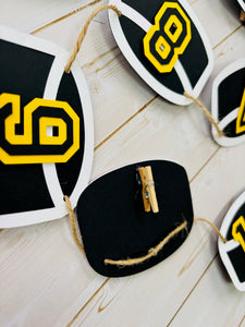 Hockey puck first birthday photo banner featuring 13 hockey pucks. Each hockey puck is sized to fit one 4x6 portrait or orientation photo. The numbers are yellow and the black. The number colors are customizable and can be matched to coordinate with your favorite hockey team colors. 