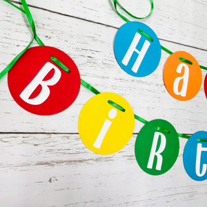 Primary colors circle pennant happy birthday banner strung on green satin ribbon. 