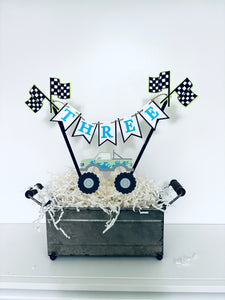 Pink monster truck cake topper. The cake topper is customizable and can display an age, name, word or phrase. The colors are also customizable. The pink monster truck cake topper features two checkered flags, pennant banner and a monster truck to display underneath the bunting. The pink monster truck cake topper is designed and handcrafted by Laura, the owner of Declan & Smith Party Decor. 
