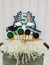 Load image into Gallery viewer, Monster jam inspired dueling monster truck cake topper. The monster jam cake topper features two monster trucks, a checkered flag, dirt mounds, age for the birthday boy or girl and the birthday kiddo&#39;s name. The monster jam cake topper is customizable. 
