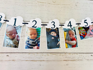 Top Gun fighter jet themed first birthday photo banner. The top gun photo banner features two fighter jets flanking 13 white clouds. The clouds are numbered NB - 12 months for a first birthday. The numbers can be customized to fit any age birthday. The planes, number colors and ribbon color is customizable. 