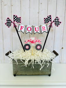 Pink monster truck cake topper. The cake topper is customizable and can display an age, name, word or phrase. The colors are also customizable. The pink monster truck cake topper features two checkered flags, pennant banner and a monster truck to display underneath the bunting. The pink monster truck cake topper is designed and handcrafted by Laura, the owner of Declan & Smith Party Decor. 