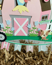 Load image into Gallery viewer, The pink barnyard farm animals cake topper features a pink barn, pink tractor, white picket fence, farm animals and a pink and light blue pennant banner to display your little one&#39;s name. 
