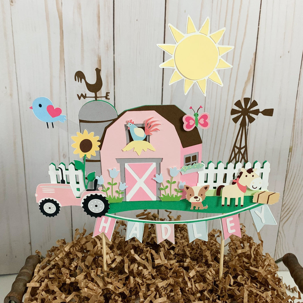 The pink barnyard farm animals cake topper features a pink barn, pink tractor, white picket fence, farm animals and a pink and light blue pennant banner to display your little one's name. 