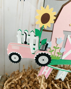 The pink barnyard farm animals cake topper features a pink barn, pink tractor, white picket fence, farm animals and a pink and light blue pennant banner to display your little one's name. 