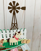 Load image into Gallery viewer, The pink barnyard farm animals cake topper features a pink barn, pink tractor, white picket fence, farm animals and a pink and light blue pennant banner to display your little one&#39;s name. 
